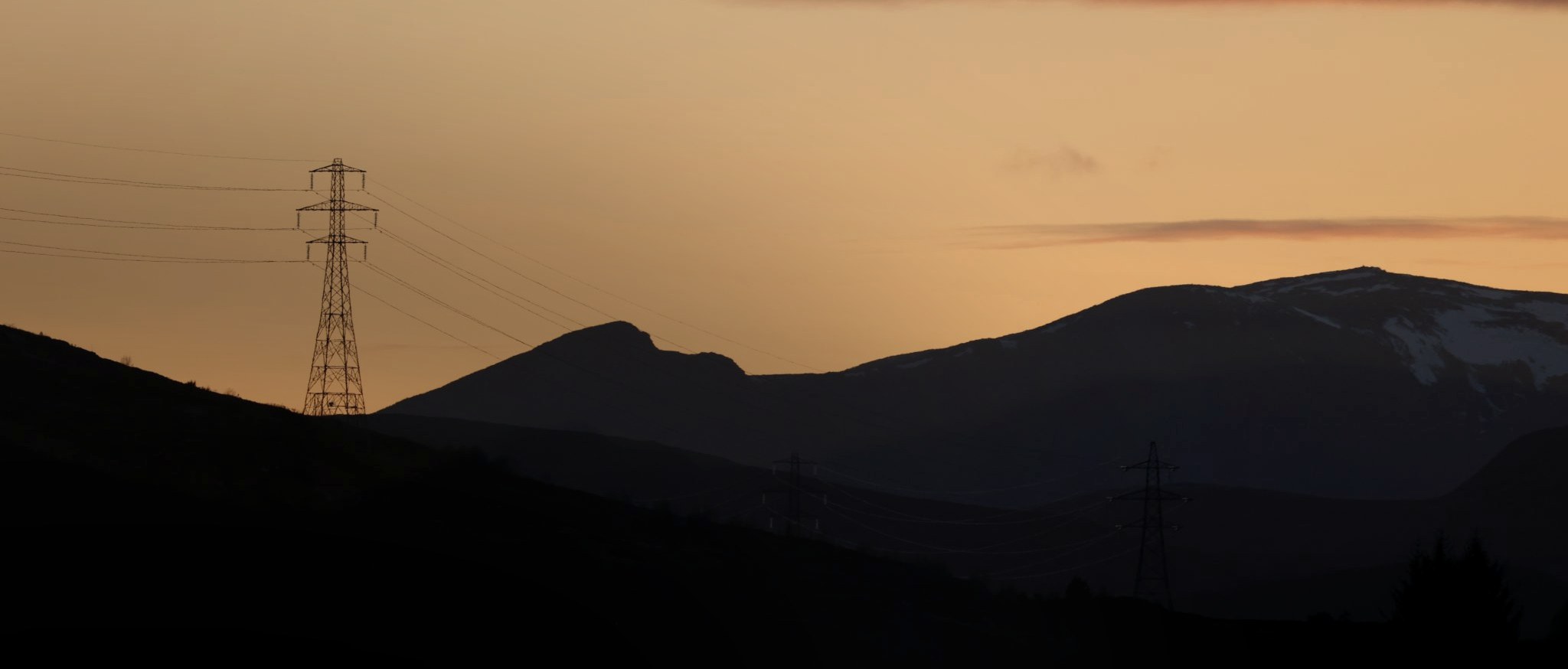 Transmission pylons silhouetted against a dusk sky over distant hills